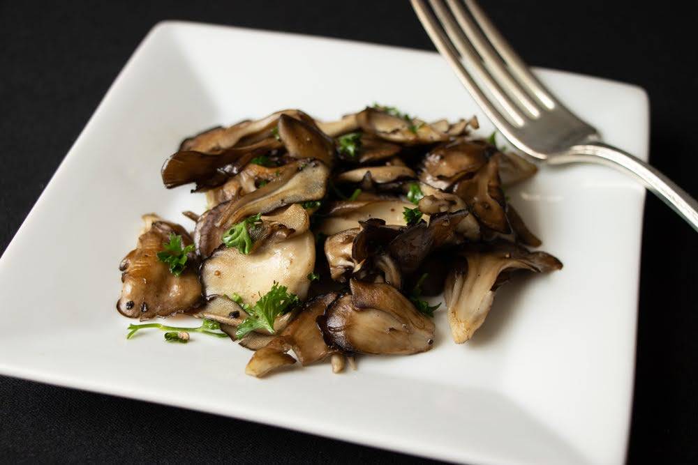 Sauteed maitake mushrooms on a plate with a fork to the side.